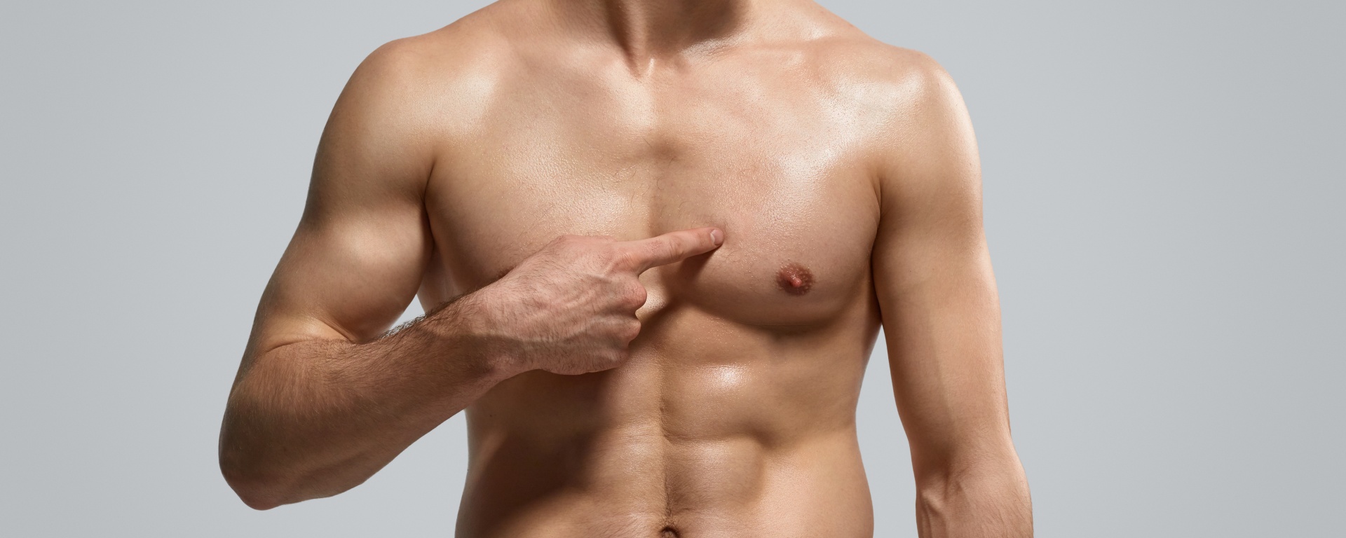 Anonymous shirtless athlete pointing at pectoral muscle after workout against gray background