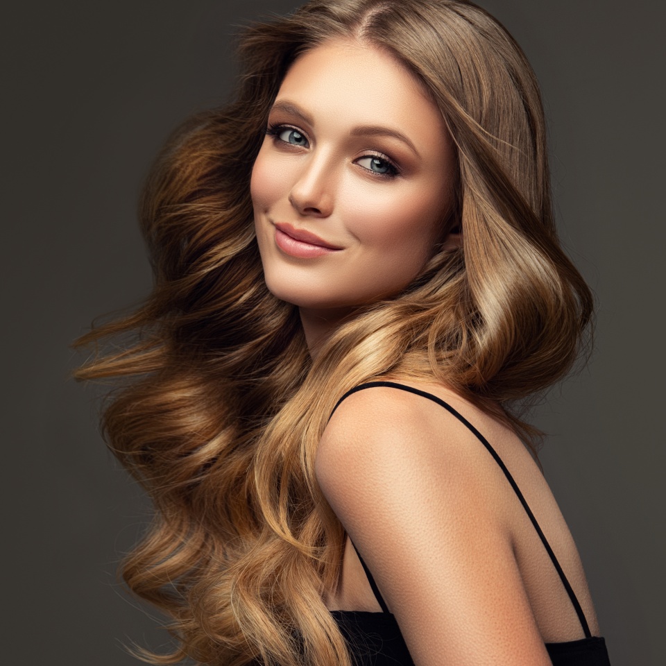 Beauty blonde girl with long and shiny wavy hair . Beautiful woman model with curly hairstyle . Fashion, cosmetics and makeup