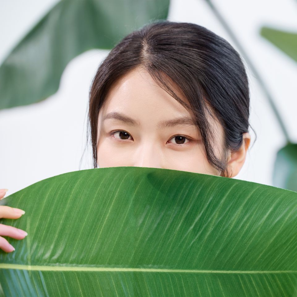 A woman ashamed of scarring hiding lower part of her face behind a big tropical plant leaf